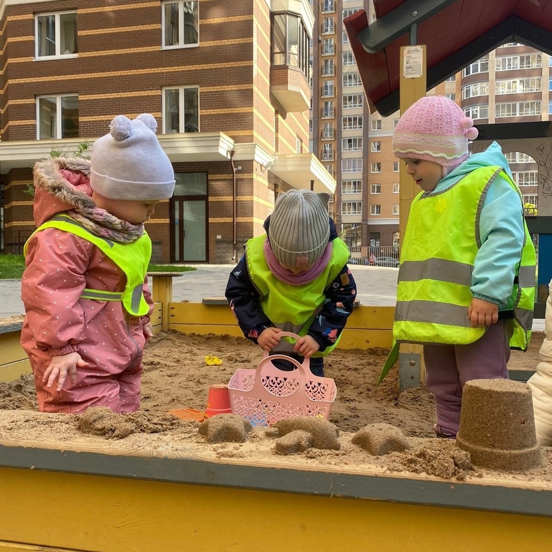 Малыши дружно играют в песочнице на детской площадке садика 